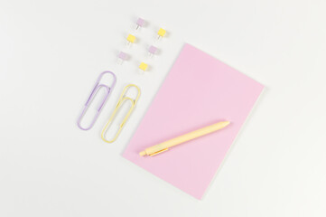 Top view of pink notebook on white background. Paperclips, pen and pins. School, office wallpaper. Flat lay, copy space.