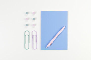 Top view of blue notebook on white background. Paperclips, pen and pins. School, office wallpaper. Flat lay, copy space.