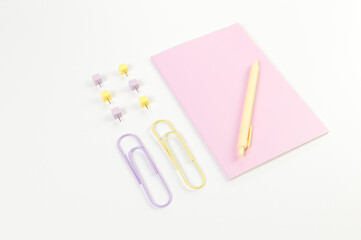 Top view of pink notebook on white background. Paperclips, pen and pins. School, office wallpaper. Flat lay, copy space.