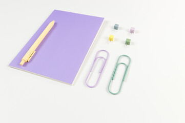 Top view of purple notebook on white background. Paperclips, pen and pins. School, office wallpaper. Flat lay, copy space.