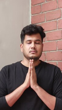 indian man ih 30s is doing prayer by joining two hands in anjali mudra, prayer position. his eyes are closed and he is meditating by chanting the name of his god. meditating fof calm mind and happines