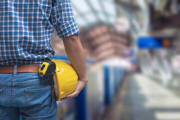 Close-up of a construction worker holding a yellow hard hat and tape measure, standing inside a modern building.