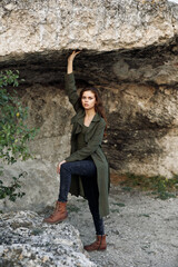 stylish woman in green coat and boots striking pose on rock against tree background