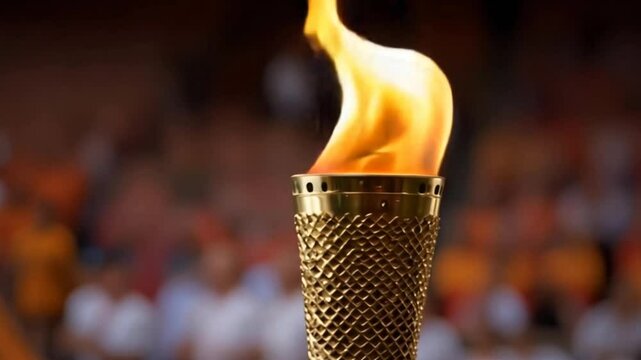 A close-up view of a lit Olympic torch held high above a crowd of spectators. The flame burns brightly, a symbol of the Olympic Games