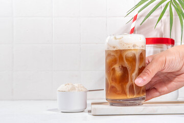 Collagen latte coffee drink glass with collagen powder in jar and spoon, on white kitchen table. Natural supplement for beauty, health of skin, bones, joints and intestines, anti-age concept