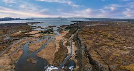 Stunning aerial image of Pingvellir National Park in Iceland, showcasing the rift valley, winding road, small lake, and a picturesque waterfall.