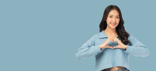 Smiling young asian woman showing heart gesture by using two hands and looking at camera isolated over blue background copy space 