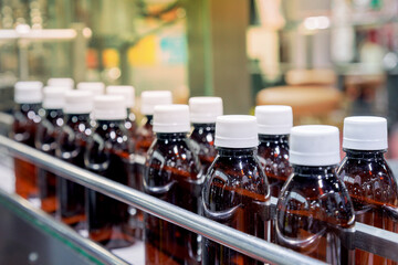 glass bottle with white cap moving on conveyor belt of auto capping and labeling machine at energy drink beverage manufacturing. pharmaceutical or beverage industry. automation technology machinery.