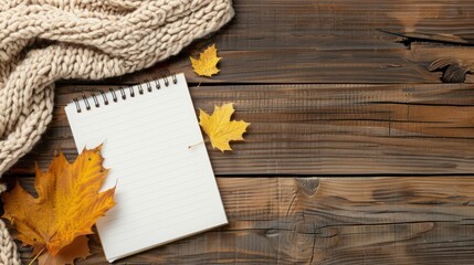 A notebook with a leaf on top of it. The notebook is open to a blank page. The leaf is yellow and brown