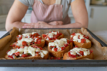 Woman with fresh and homemade baked bruschetta with tomatoes and mozzarella cheese on a baking tray
