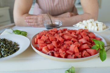 Preparing a fresh watermelon salat with feta cheese and pumpkin seeds by woman´s hands. Healthy homemade summer food