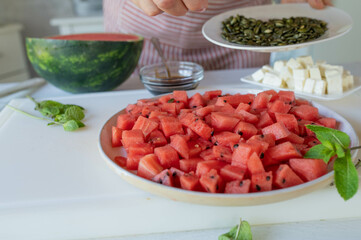 Homemade summer food. Woman preparing a fresh salad with watermelon, feta cheese and pumpkin seeds