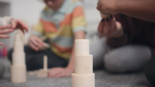 Close-up of hands of preschool children spending time at daycare centre playing with wooden educational toys, making pyramids and tower under guidance of female teacher