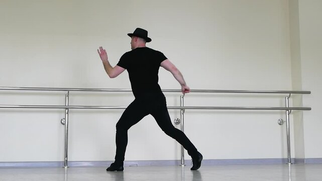  Jazz dance or caberet rehearsal in the studio by a young guy in a gangster hat. Creative dance blues mena. A dancer in black clothes makes beautiful swings with his legs