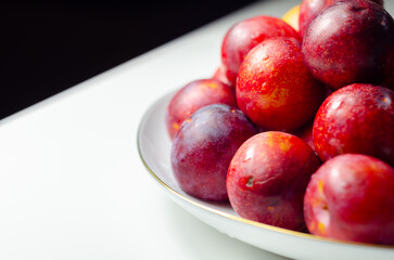 A white plate with a bunch of red plums on it