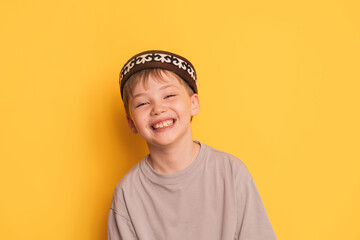 Smiling boy in a Kazakh skullcap in front of a yellow background.