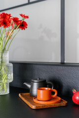 Closeup on orange cup with saucer and ceramic teapot on wooden tray at kitchen