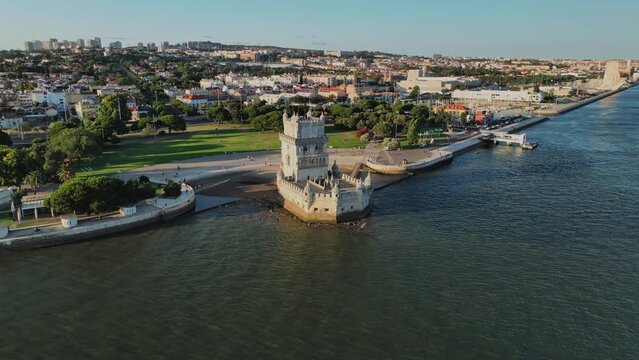 Aerial drone view of Belem Tower famous tourist landmark of Lisboa and tourism attraction on the bank of the Tagus River (Tejo) with tourist boat at sunset. Lisbon, Portugal. Orbit parallax shot
