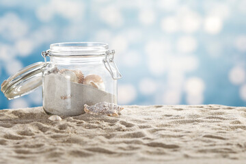 Jar with seashells and holiday souvenirs from a sandy beach. In the background, blurred sea...