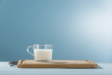 A glass cup of milk on wooden cutting board with bright table and blue wall background.