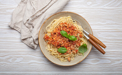 Plate of delicious spaghetti bolognese with fresh basil leaves, served on a rustic wooden table