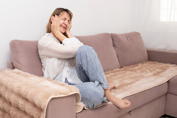 Young beautiful woman sitting on sofa and crying at home