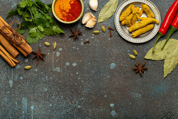Turmeric root, cinnamon sticks, bay leaves and other spices traditional for Indian cuisine creating a frame on dark background