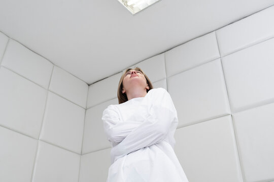 Young frustrated girl in a straitjacket is in an isolated white room in a mental hospital	