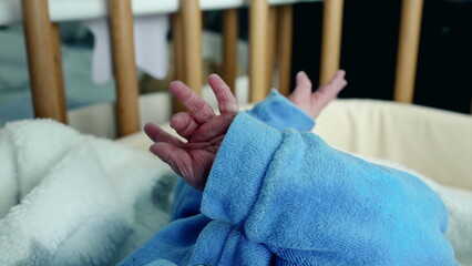 Newborn baby in blue onesie, close-up of tiny hand reaching out, soft blanket, wooden crib, delicate fingers, infancy, early life, capturing innocence, peaceful rest, serene moment