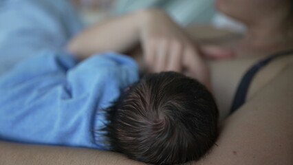 Close-up of a newborn breastfeeding in a hospital bed, wrapped in a blue blanket, highlighting the tender and intimate connection between mother and child during feeding