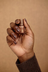 Vertical shot of Black woman holding golden nail polish for creating manicure. Dark brown nails...