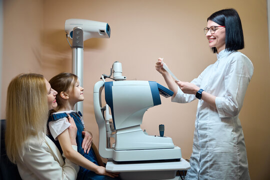 Mother and her little daughter are sitting at an autorefractometer