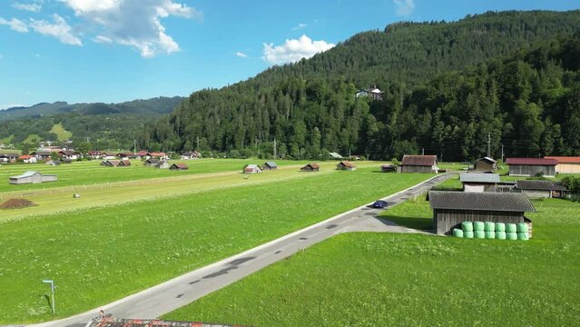 chasing car near wooden huts garmisch partenkirchen germany distance summer sunshine green grass field mountains hills forest dynamic aerial