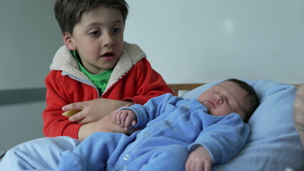 Young sibling holding hands with sleeping newborn baby, representing family bonding, love, and...
