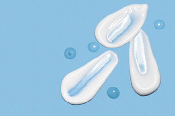 creamy smears and drops of serum or serum cosmetic texture on blue background with space for text