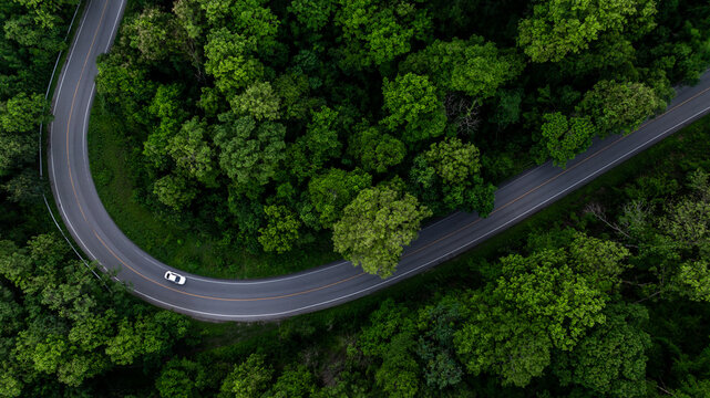 Aerial view electric vehicle car driving on asphalt road in mountain green forest, EV car electric vehicle car on forest road green energy and eco power, White electric car driving green forest road.