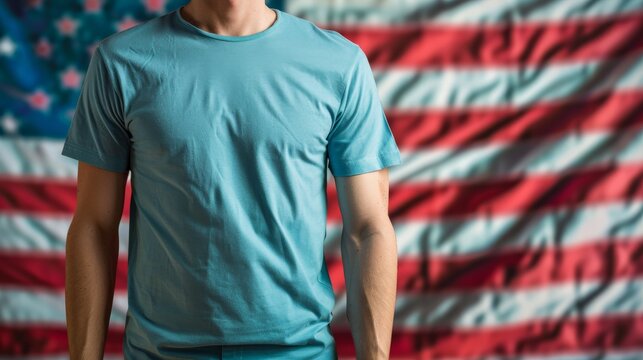 A man wearing a blank blue T-shirt in front of a blurred American flag