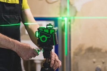 Builder is measures the repair lines for laying tiles using a laser level with green beams. Close up.