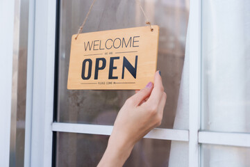 Beautiful Asian girl small business spa owner placing open sign on door. Wearing blue apron and light blue shirt, ready to welcome customers. Professional, clean, inviting spa environment.