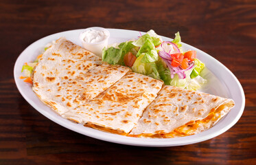 Quesadillas on a white plate with salad and sour cream on a dark wooden table; copy space