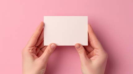 Fototapeta premium Hands holding a blank white business card on a pink background. Mock-up template for branding, business, and identity design concepts.
