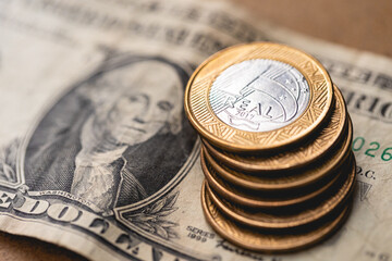 Real Brasileiro e Dólar americano. Uma pilha de moedas brasileiras de 1 Real sobre uma nota de 1 dólar dos Estados Unidos. Câmbio, inflação, desvalorização e economia brasileira.