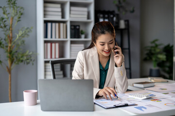 Fototapeta premium A woman is talking on her cell phone while sitting at a desk with a laptop