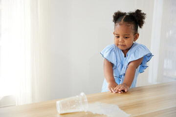 Fototapeta premium little African girl spilling milk and feeling sad on the table