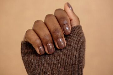 Close up shot of simple nail design in rich brown shade for autumn complementing outfit on beige...