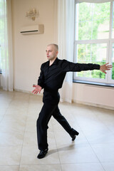 Male dancer in classic black shirt and trousers dance sports ballroom dancing, indoors. Vertical