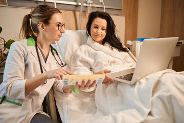 Lady patient with laptop is lying on hospital bed