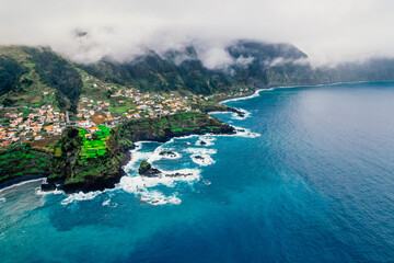 Obraz premium Aerial view of rough ocean with waves, volcanic beach and swiming pool in Seixal, Madeira, Portugal