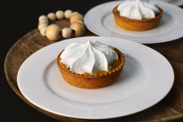 Lemon tart with zingy lemon curd topped with whipped lemon cream on white plate on wooden tray
