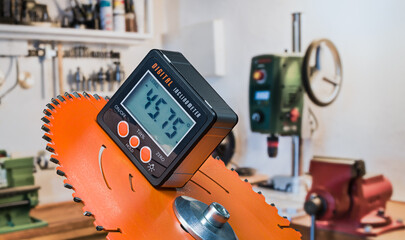 Electronic inclinometer with digital display on orange disc of power miter drop saw. Closeup of precise tool for measuring slope angle and bench vice, drilling machine or lathe on workroom background.